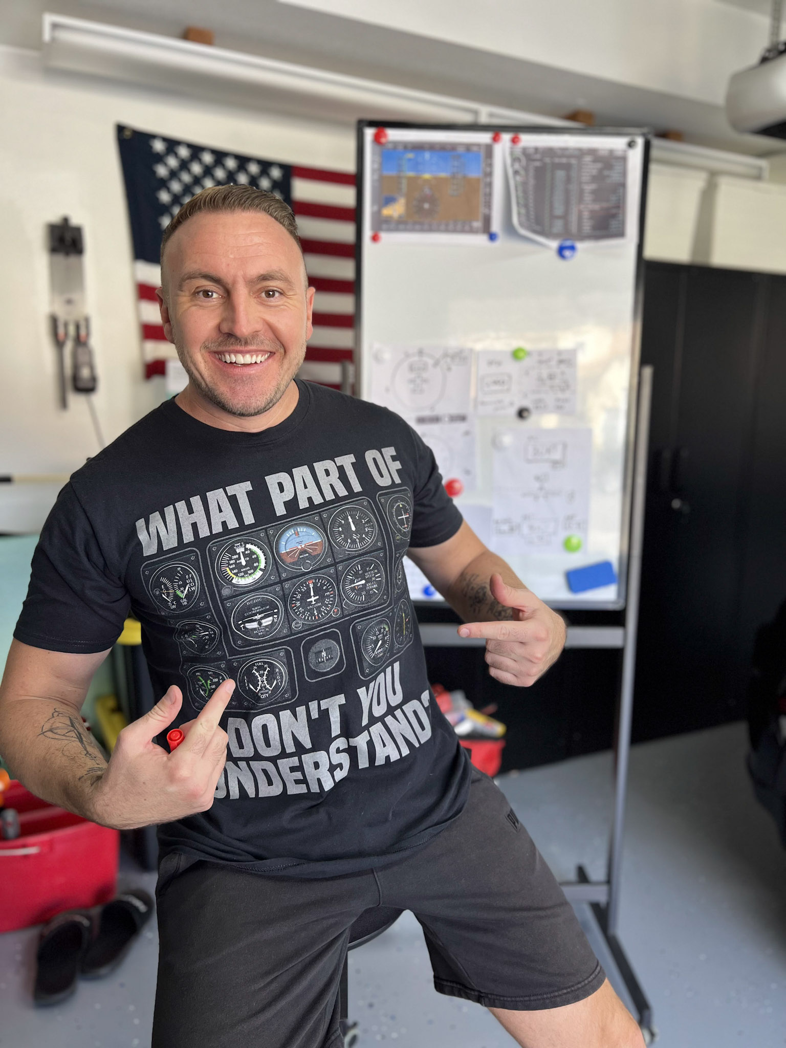 Dennis Schaefer wearing a cockpit instruments t-shirt, pointing at flight planning materials on a whiteboard
